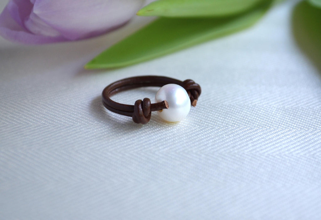 Pearl ring on a white fabric background with a blurred flower in the background