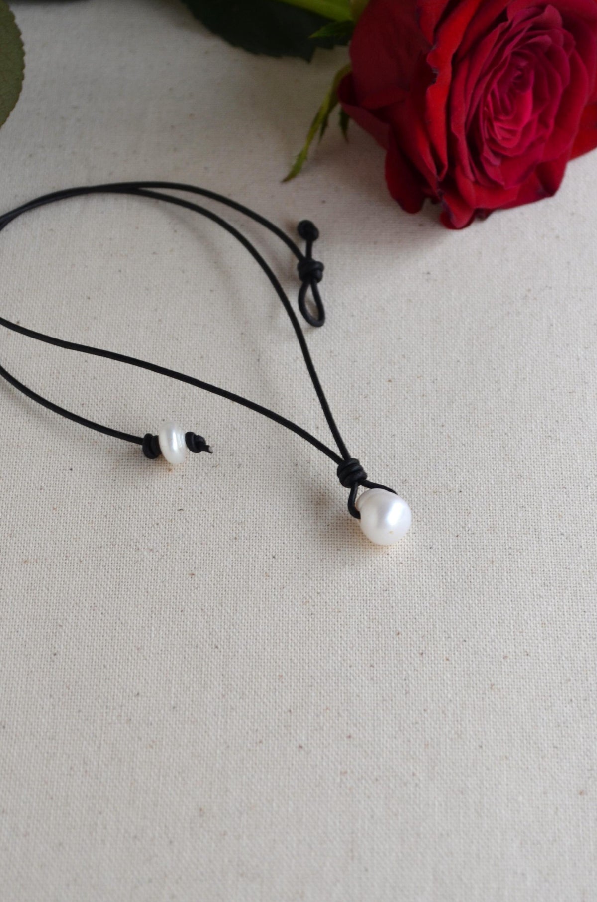 Pearl necklace on a beige surface with a red rose in the background