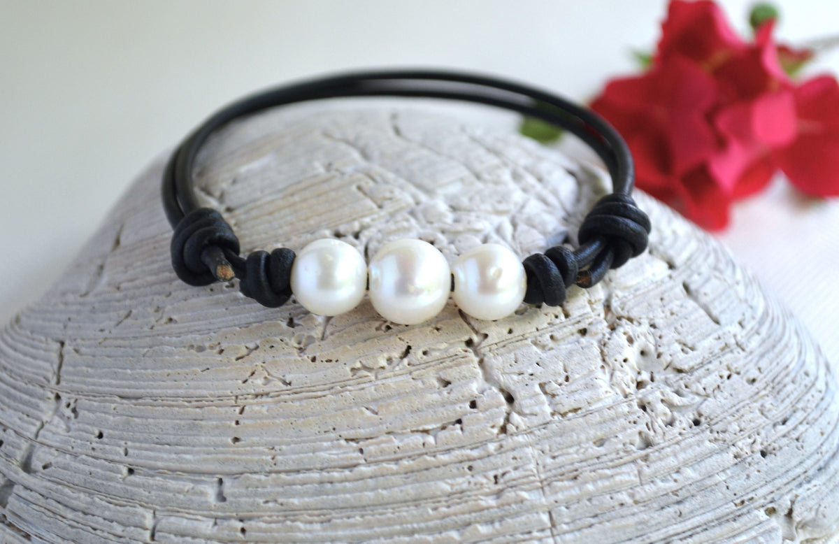 Bracelet with three white freshwater pearls on a textured surface with red flowers in the background