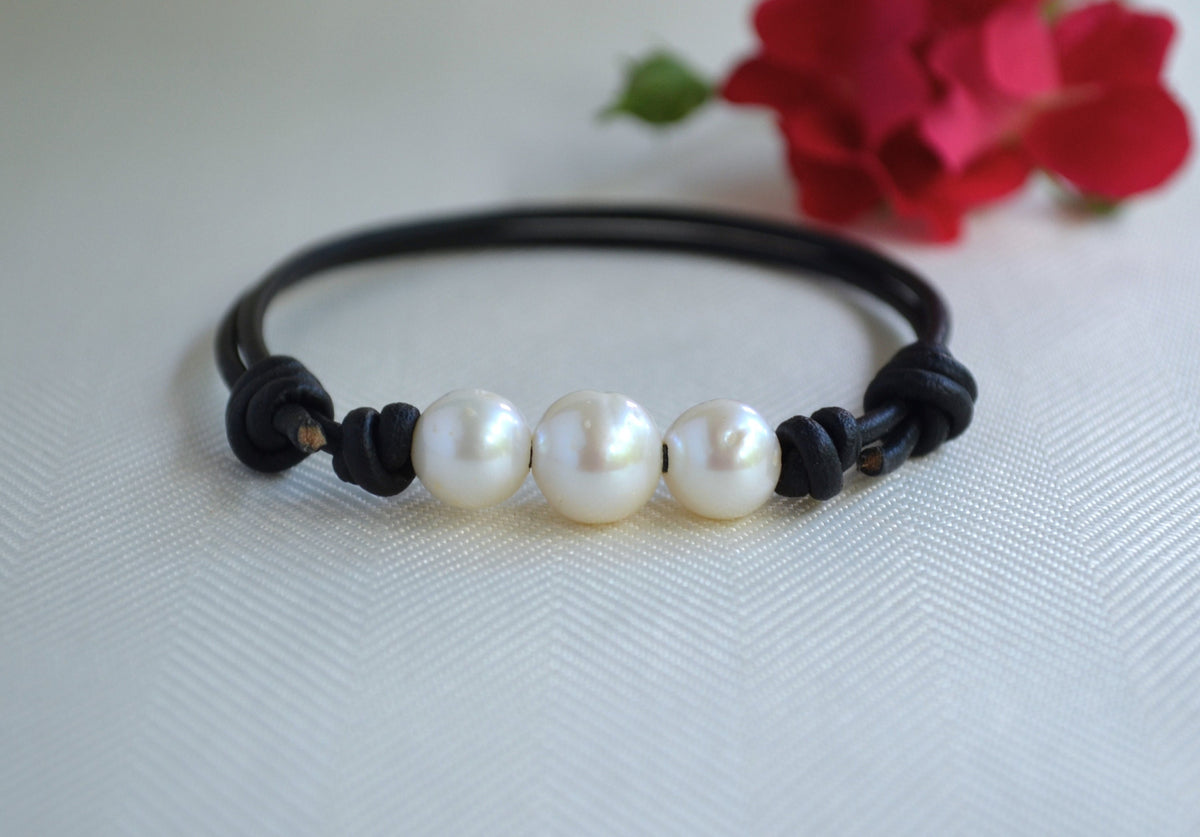  Leather bracelet with three pearls on a white background with red flowers.