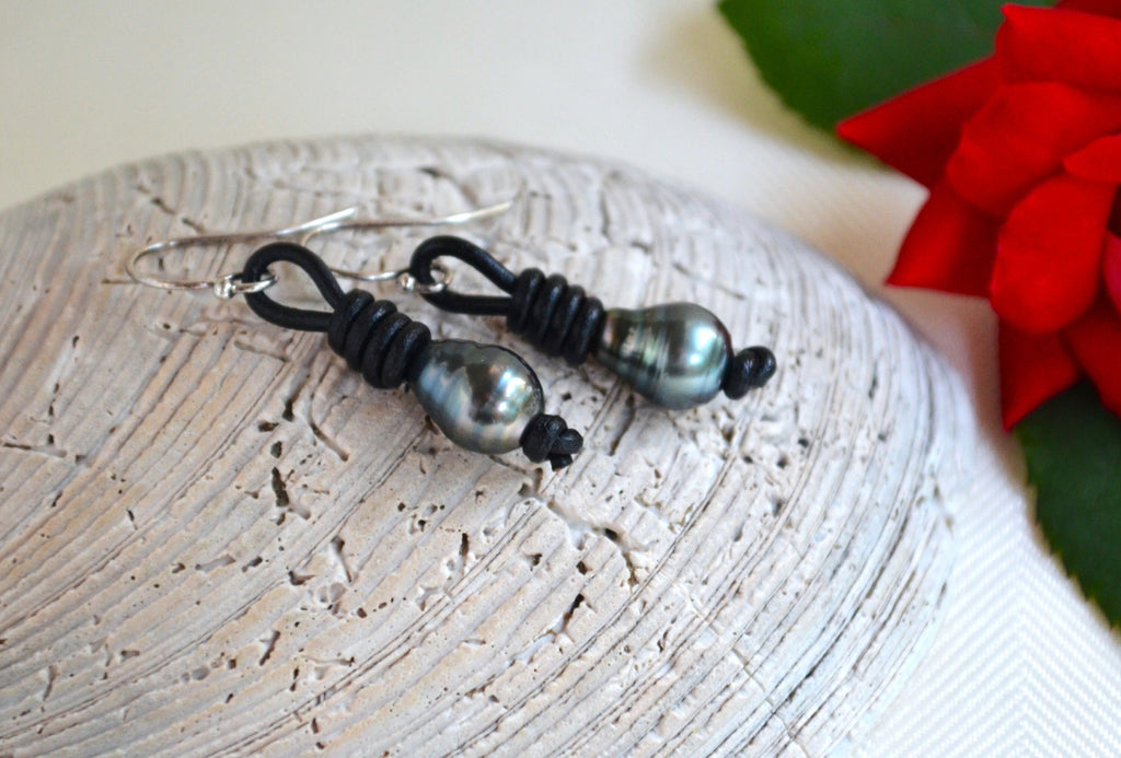 Pair of black Tahitian pearls beaded earrings on a textured surface with a red flower in the background