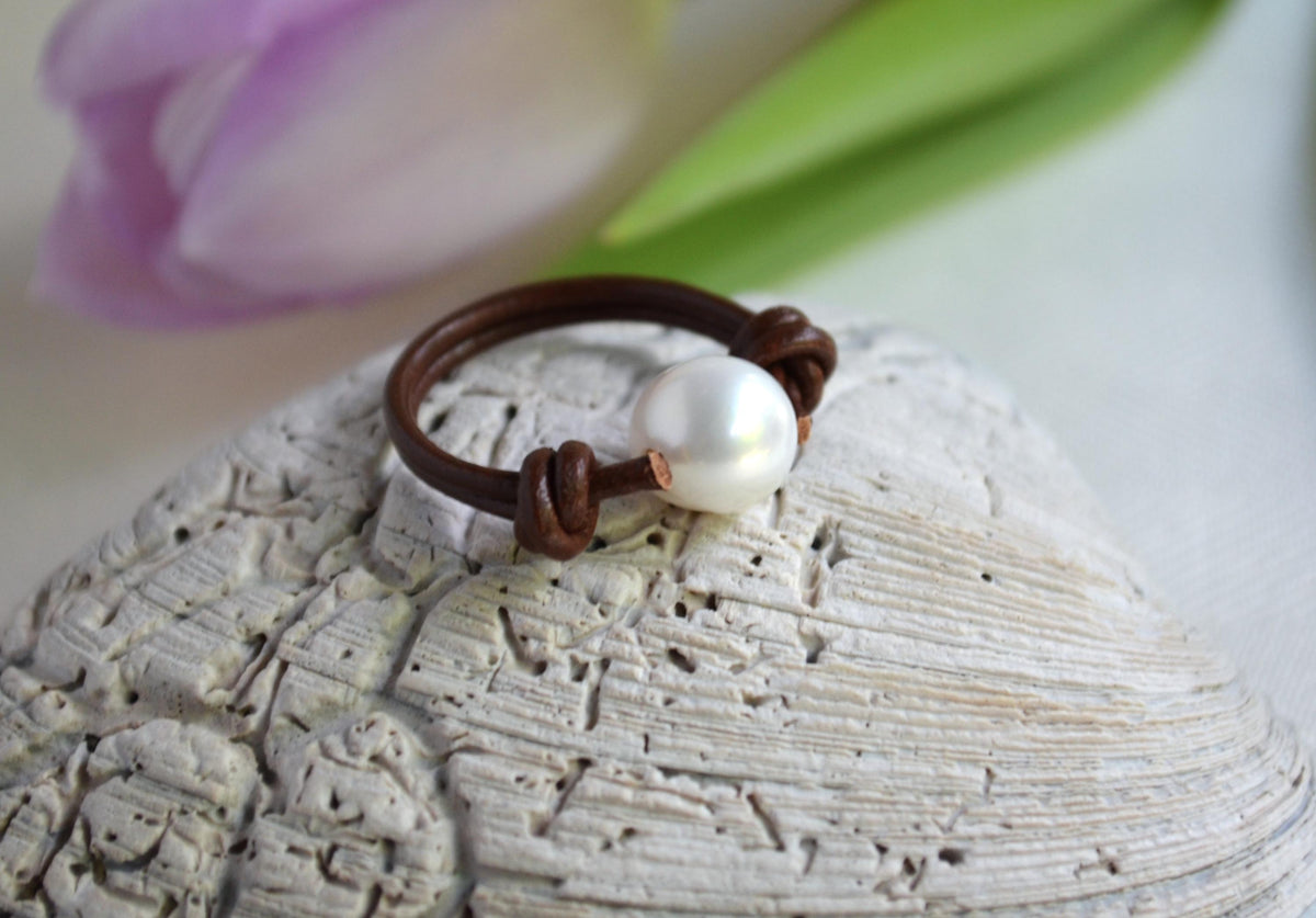 Pearl ring on a textured stone surface with blurred floral background