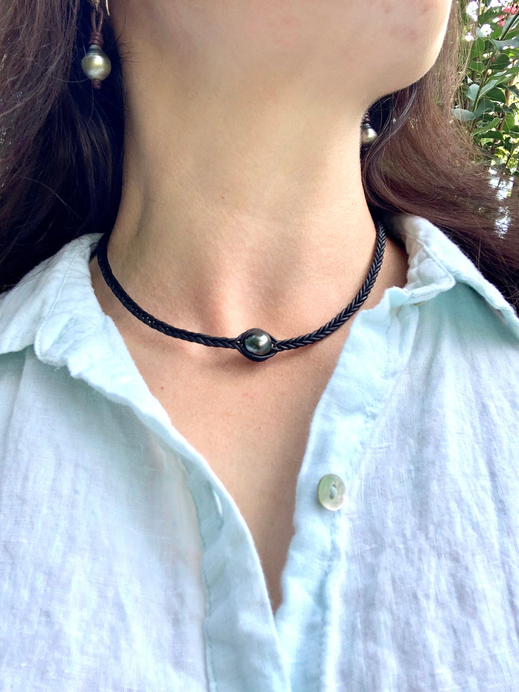 Person wearing a black cord necklace with a pendant, close-up on neck and shoulders.